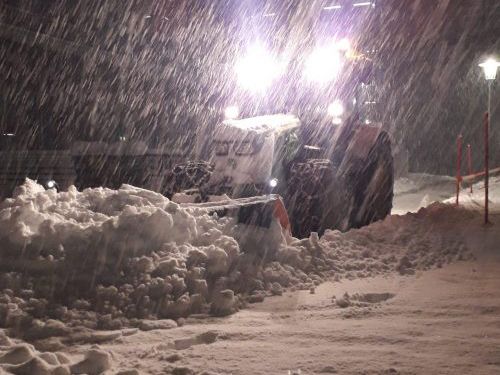 Räumfahrzeug mit Schneeschild schiebt bei Nacht und starkem Schneefall Schnee zusammen